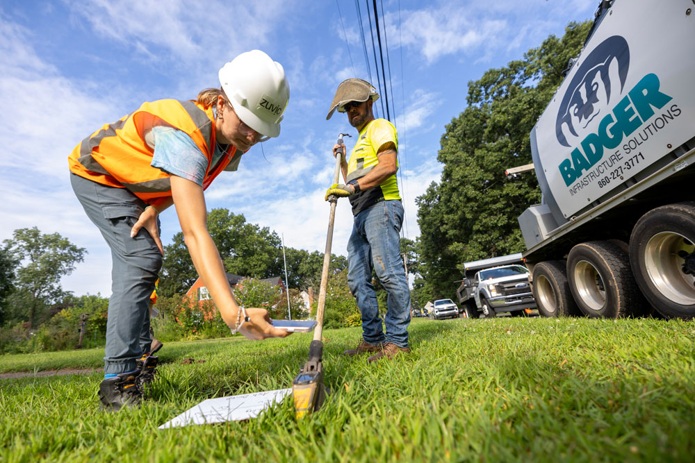 A team visually inspects a water service line after excavating a hole to see it.