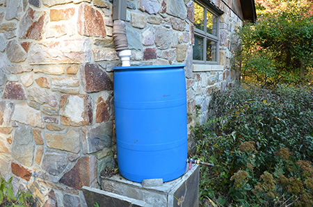 a blue rain barrel connected to a house gutter system